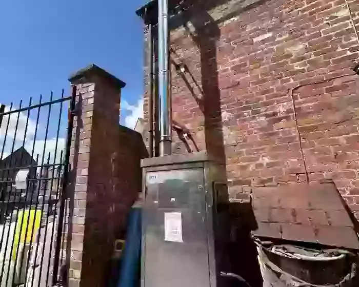Nilfisk DTE static pressure washer fitted with a stainless steel flue extension at a brewery in Burton, installed to safely redirect boiler exhaust fumes away from a confined courtyard cleaning area.